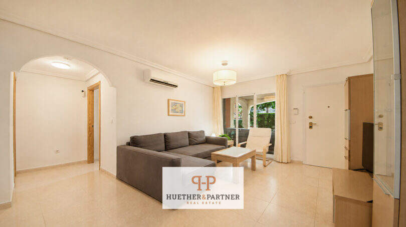 Helles Wohnzimmer der Erdgeschosswohnung Cala Antena mit L-Sofa, Klimaanlage und Terrassenzugang