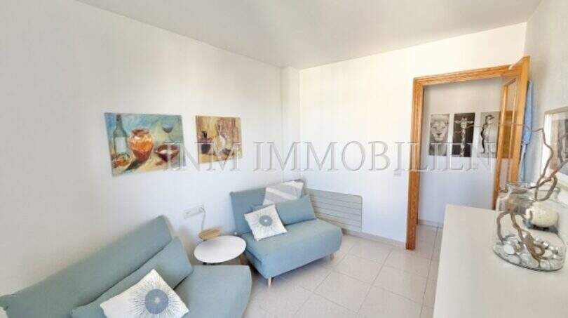 Helles Wohnzimmer mit türkisfarbenem Sofa, Sessel und dekorativen Gemälden in Wohnung in Palmanova