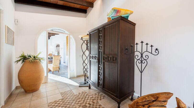 Entrance area of the sea view villa in Cala Murada with wooden beam ceiling, dark wooden cabinet and barrel arch.