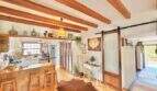 Área abierta de sala y comedor con techo de vigas de madera, mostrador de cocina y puerta corredera en casa mediterránea Sa Ràpita