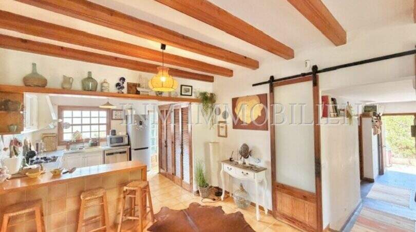 Área abierta de sala y comedor con techo de vigas de madera, mostrador de cocina y puerta corredera en casa mediterránea Sa Ràpita