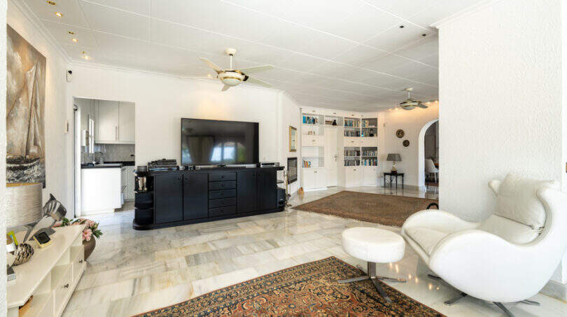 Helles Wohnzimmer der Poolvilla in Cala Murada mit Marmorboden, großem TV, Designsessel und Bücherregal.