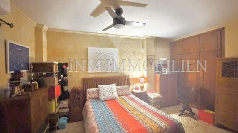 Helles Schlafzimmer der Palma-Wohnung mit Deckenventilator, bunter Tagesdecke und Holzschrank