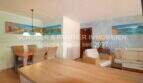 Helles Wohn- und Esszimmer der Poolwohnung in Sa Coma mit Holztisch, Rattanstühlen und mediterraner Wanddekoration.