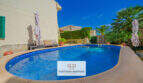 Ovaler Pool mit Poolumrandung, Sonnenschirmen und Palmen im Garten des Ferienhauses in Cala Murada.