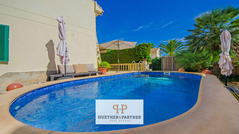 Ovaler Pool mit Poolumrandung, Sonnenschirmen und Palmen im Garten des Ferienhauses in Cala Murada.