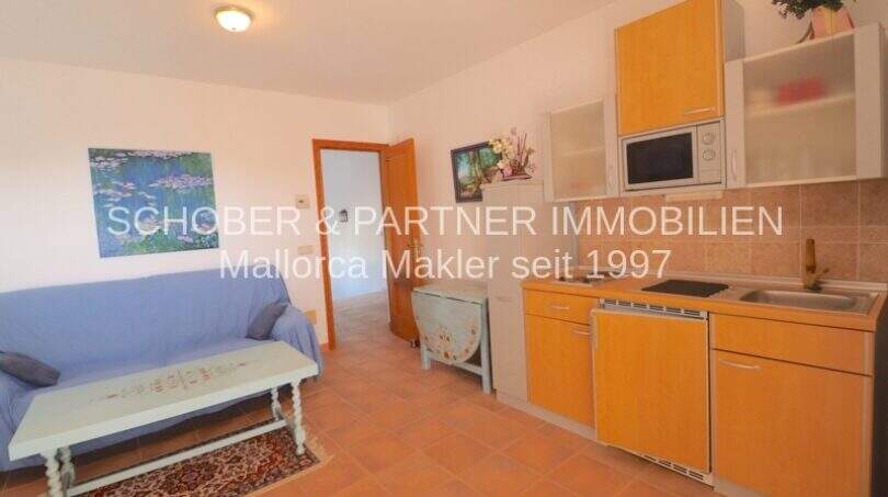 Helles Studio-Apartment mit Küchenzeile, blauem Sofa und Terrakottaboden im OG des Chalets in Sa Coma.