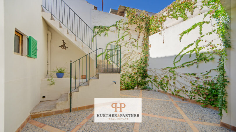 Sonniger Innenhof mit Natursteinpflaster, begrünten Wänden und Außentreppe eines Stadthauses in Manacor