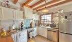 Cocina mediterránea con techo de vigas de madera, armarios blancos y electrodomésticos de acero inoxidable en casa Sa Ràpita