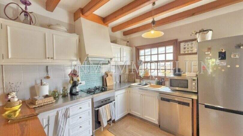 Cocina mediterránea con techo de vigas de madera, armarios blancos y electrodomésticos de acero inoxidable en casa Sa Ràpita