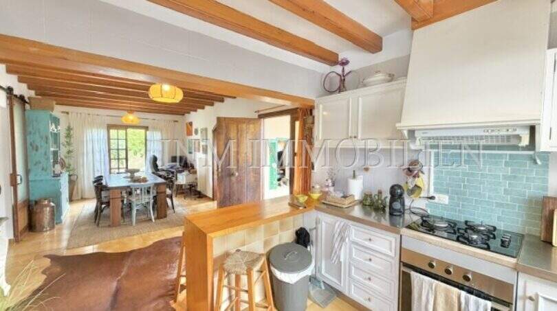 Cocina abierta con techo de vigas de madera, isla de cocina y vista al comedor en casa mediterránea Sa Ràpita