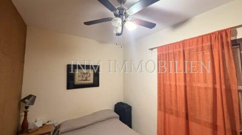 Schlafzimmer der Palma-City-Wohnung mit Doppelbett, Deckenventilator und orangefarbenem Vorhang