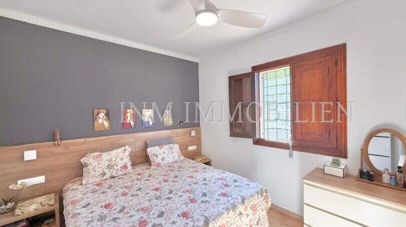Schlafzimmer der Finca Algaida mit Doppelbett, Holzkopfteil, Deckenventilator und rustikalem Holzfenster