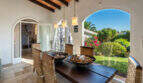 Covered terrace with dining table, wicker chairs and view into the Mediterranean garden of the villa in Cala Murada
