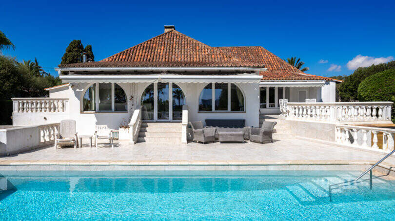 Mediterrane Poolvilla in Cala Murada mit Terrasse, Lounge-Bereich und rotem Ziegeldach unter blauem Himmel.