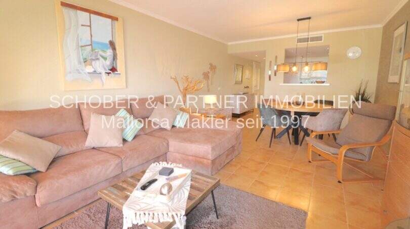 Luminosa sala de estar con sofá, mesa de centro y comedor abierto en un apartamento de 4 habitaciones en Cala Millor