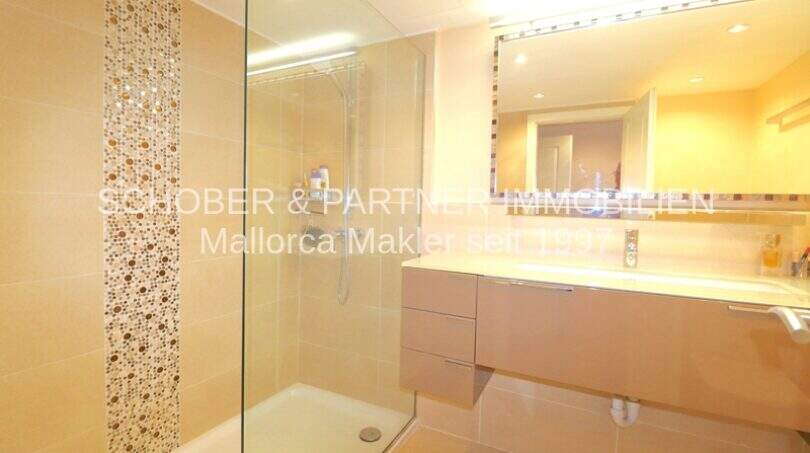 Baño moderno con ducha de plato sin escalón de vidrio, pared con revestimiento de mosaico y elegante lavabo en apartamento Cala Millor