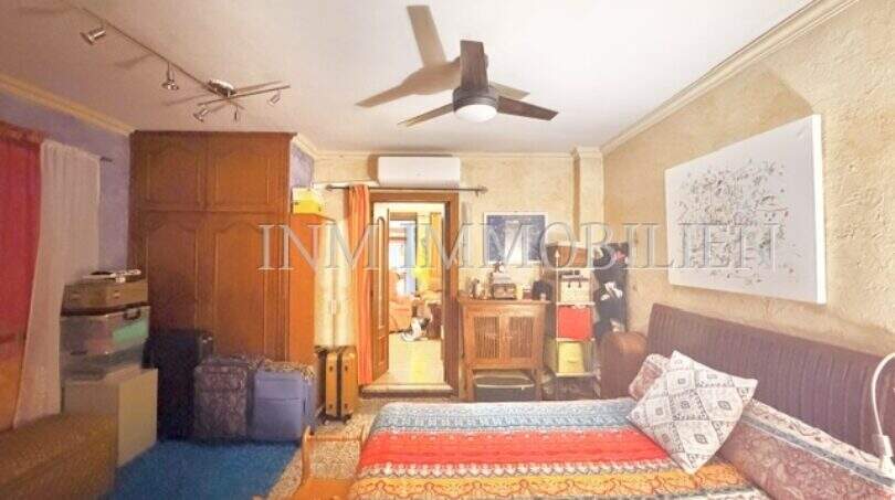 Schlafzimmer der Wohnung in Palma mit bunter Tagesdecke, Holzschrank, Deckenventilator und Klimaanlage.