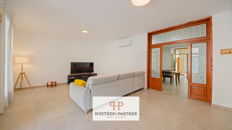 Helles Wohnzimmer mit grauem Sofa, TV und eleganten Holzglastüren zum Esszimmer im Stadthaus Manacor
