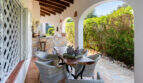 Covered terrace of the sea view villa in Cala Murada with rattan furniture, wooden table and view into the garden.