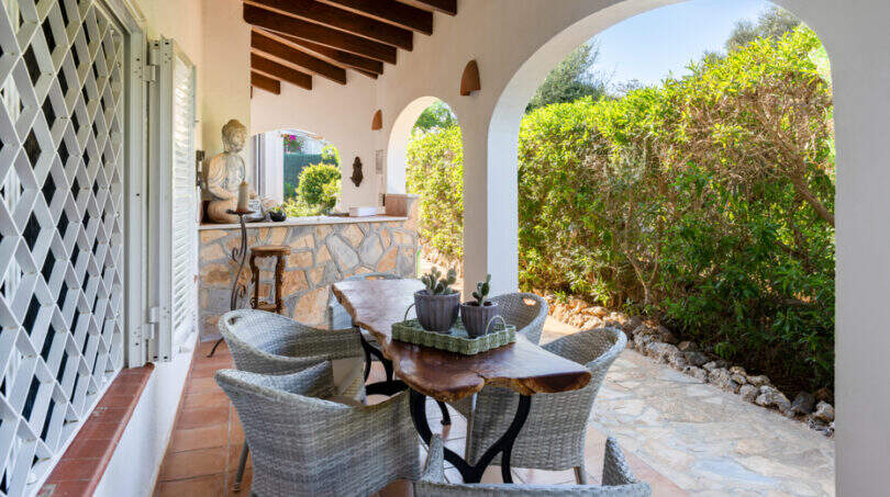Covered terrace of the sea view villa in Cala Murada with rattan furniture, wooden table and view into the garden.