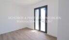 Dormitorio claro y vacío con suelo de madera y puertas-ventana negras en apartamento esquinero de nueva construcción en Cala Millor