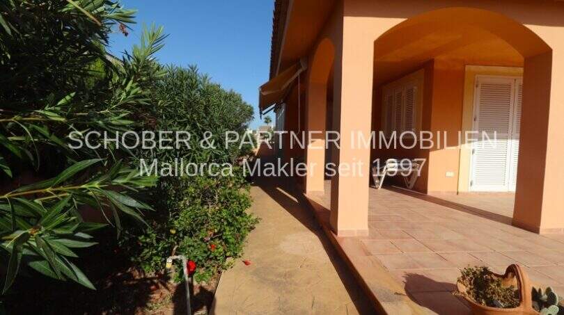 Überdachte Terrasse mit Arkaden am Chalet in Sa Coma, mediterrane Bepflanzung, Steinboden, ruhige Lage.
