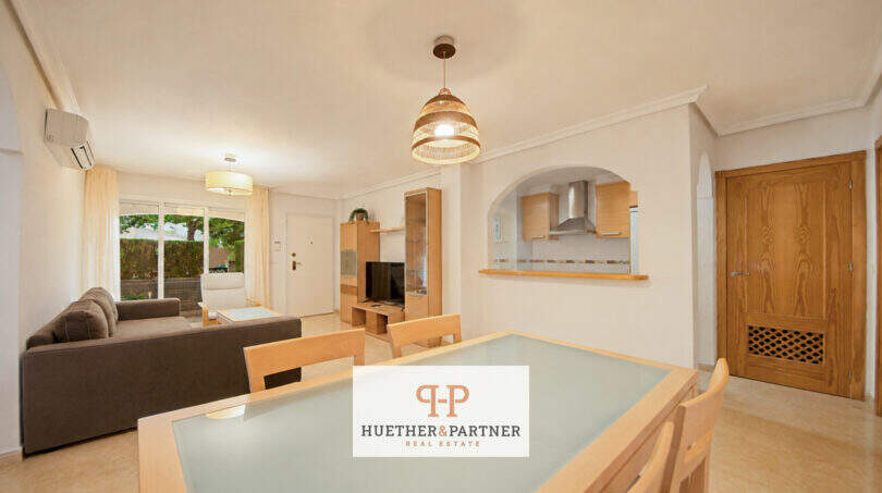 Helles Wohn-Esszimmer der Erdgeschosswohnung Cala Antena mit offener Küche, Esstisch und Zugang zur Terrasse.