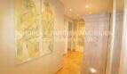 Pasillo claro con suelo de terracota, armario de madera y mural abstracto en tonos amarillos, apartamento de 4 habitaciones Cala Millor