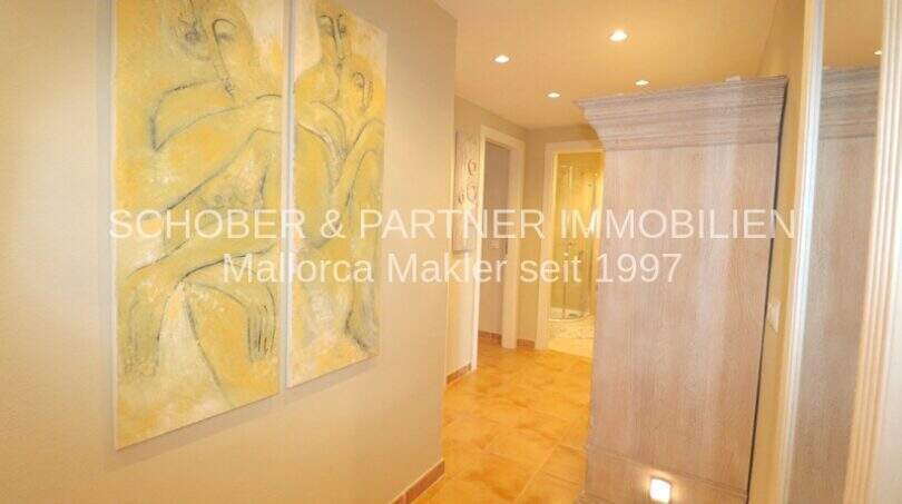 Pasillo claro con suelo de terracota, armario de madera y mural abstracto en tonos amarillos, apartamento de 4 habitaciones Cala Millor