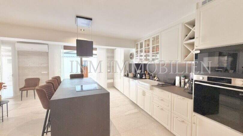 Moderne Küche mit dunkler Kochinsel, weißen Fronten und Barhockern in sanierter Wohnung in Pere Garau, Palma