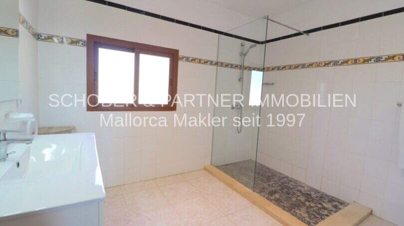 Bright bathroom of the Mallorca finca with glass shower, sink and decorative wall tiles.