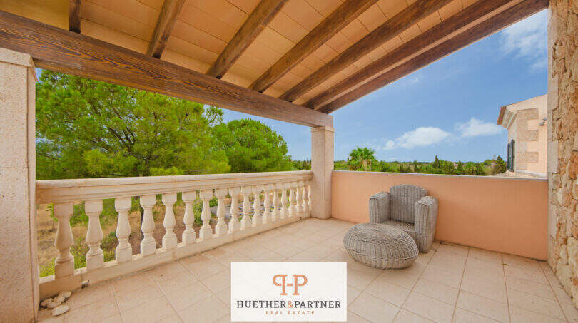 Überdachte Terrasse der Finca Santa Maria mit Holzbalken, Steinbalustrade und Blick ins Grüne.