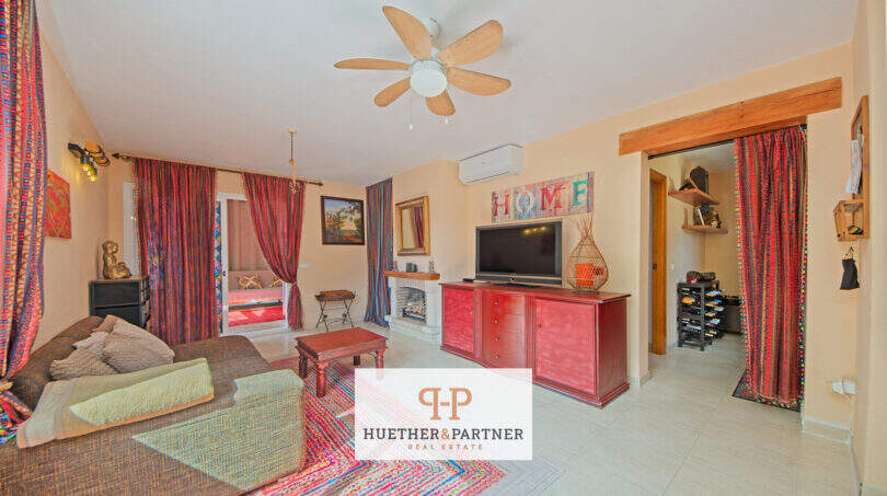 Wohnzimmer mit Deckenventilator, roter Sideboard, TV, Kamin und bunten Vorhängen in Cala Murada