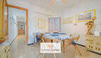 Luminoso comedor con sillas de ratán, mantel azul, ventilador de techo y cuadros en la pared en apartamento de playa Porto Cristo