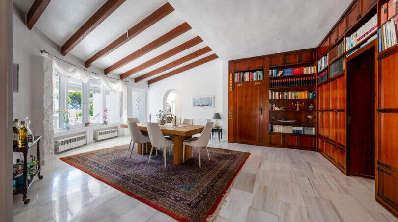 Elegantes Esszimmer mit Holzbalkendecke, Marmorboden, großer Bibliothek und orientalischem Teppich in Villa Cala Murada