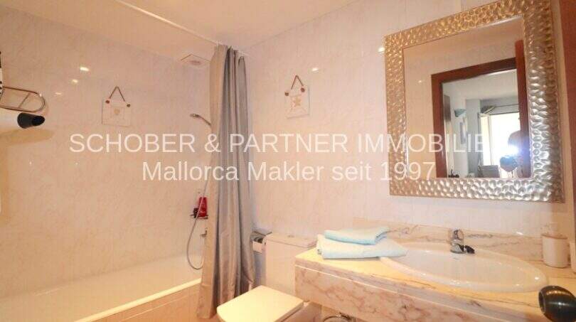 Helles Badezimmer mit Marmor-Waschtisch, Badewanne mit Dusche und elegantem Spiegel in Wohnung Sa Coma