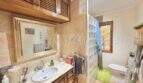 Baño con lavabo de mármol, armarios de madera, ducha de bloques de vidrio e inodoro en casa mediterránea Sa Ràpita.
