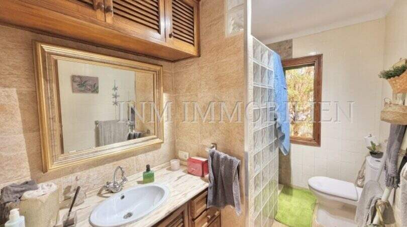 Baño con lavabo de mármol, armarios de madera, ducha de bloques de vidrio e inodoro en casa mediterránea Sa Ràpita.