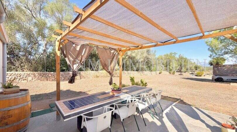 Überdachte Terrasse mit Holzpergola, Esstisch und Blick auf den mediterranen Garten der Finca bei Algaida