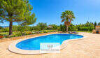 Finca Santa María: Nierenförmiger Pool mit Natursteintetrasse, Palmen und üppigem Grün unter blauem Himmel.