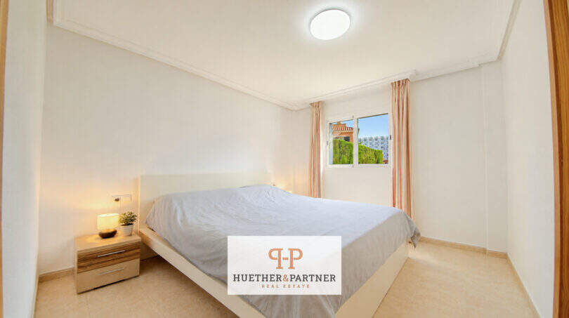 Helles Schlafzimmer der Erdgeschosswohnung Cala Antena mit Doppelbett, Nachttisch und Fenster zum Garten.