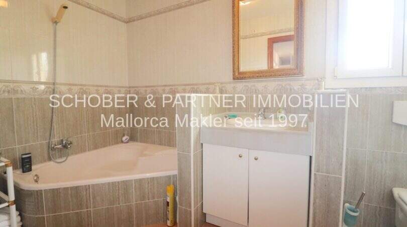 Badezimmer mit Eckbadewanne, Dusche, Waschtisch und Spiegel im Chalet Sa Coma, nahe Strand.