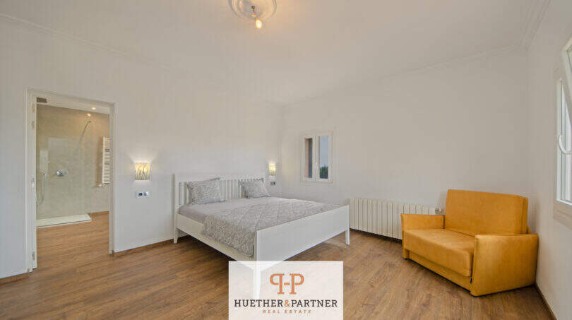 Helles Schlafzimmer der Finca Santa Maria mit Doppelbett, Laminatboden, En-suite-Bad und gelbem Sessel.