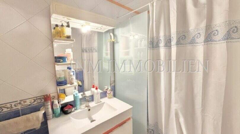 Badezimmer der Wohnung in Palma mit Waschbecken, Spiegel mit Ablage und Dusche mit Vorhang