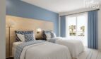 Dormitorio luminoso con dos camas, diseño de pared azul y vista al mar en el Hotel-Apartment Portocolom