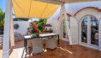 Covered terrace with rattan furniture, yellow sun sail and Mediterranean garden of the sea view villa in Cala Murada