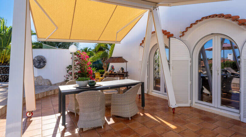 Covered terrace with rattan furniture, yellow sun sail and Mediterranean garden of the sea view villa in Cala Murada