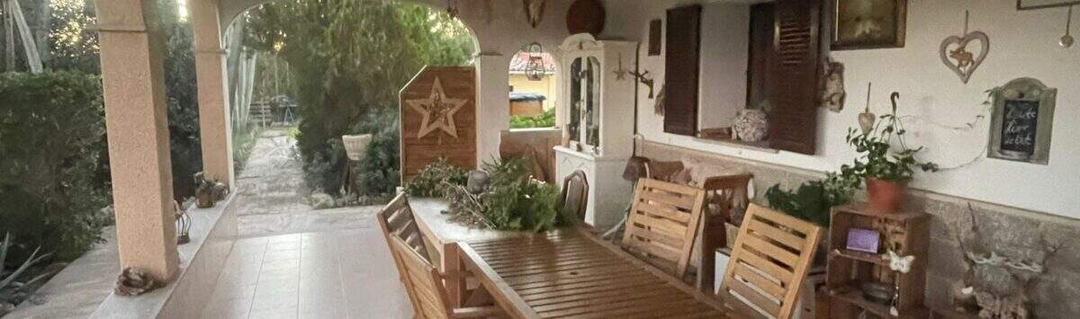 Überdachte Terrasse der Finca mit Holztisch, Stühlen und dekorativen Wandobjekten im mediterranen Stil.
