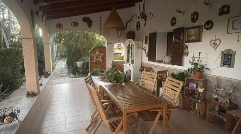 Überdachte Terrasse der Finca mit Holztisch, Stühlen und dekorativen Wandobjekten im mediterranen Stil.